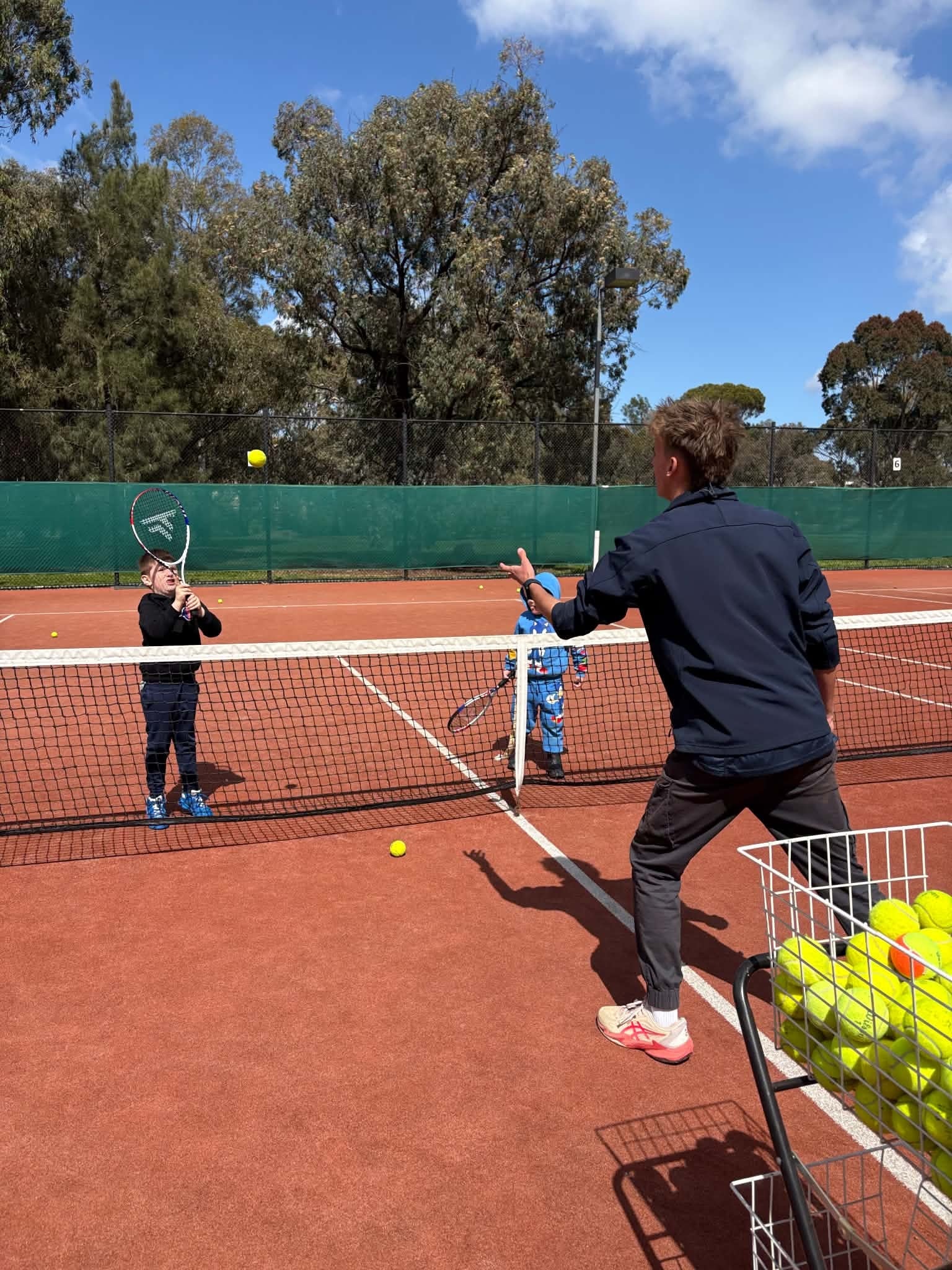 Coach teaching children tennis on the clay courts