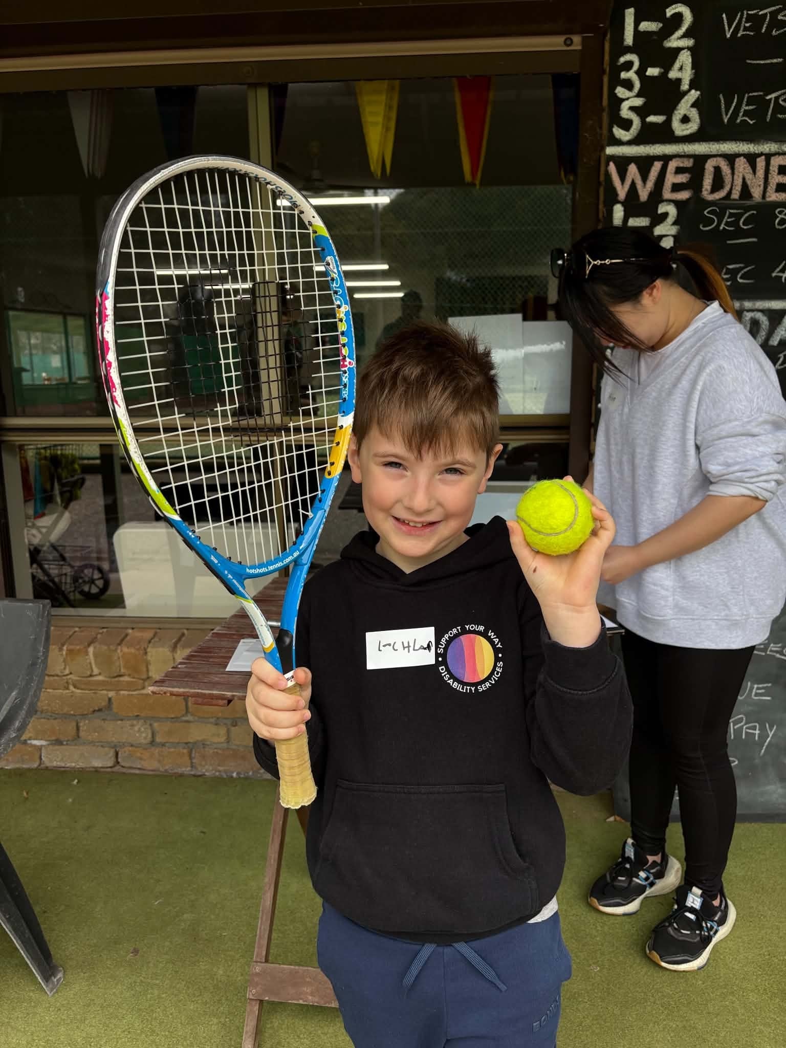Young boy holding a tennis racket and ball at the club